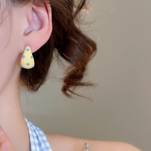 Close-up of yellow water-drop earrings with blue polka dots worn by a model