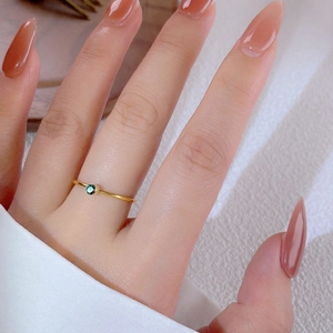 Minimalist gold titanium ring with a round emerald green gemstone on a female finger