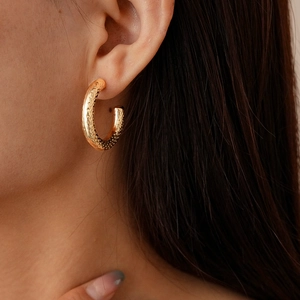Close-up of golden geometric C-shaped earrings with unique hammered texture on model
