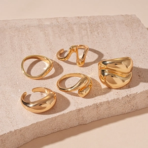Detail of 5-piece gold liquid metal rings set displayed on a natural textured stone