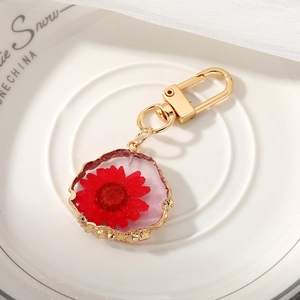 Detailed macro view of a red dried flower pendant keychain with a gold frosted metal rim