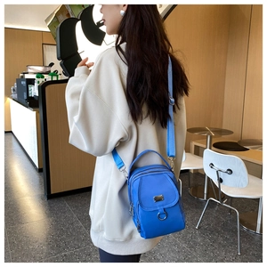 Detail of royal blue nylon crossbody bag featuring multiple zipper pockets and wide strap
