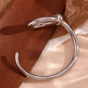 Detail of silver twisted knot open bangle on rustic wood and neutral fabric background