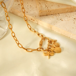 Dettaglio della collana a catena dorata con ciondoli ananas e libellula su fondo di pietra