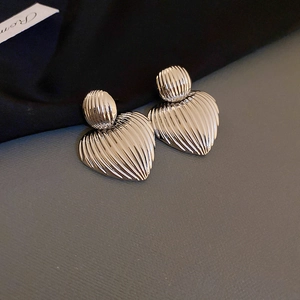 Macro detail of silver heart earrings featuring elegant vertical wavy textures and fold finish