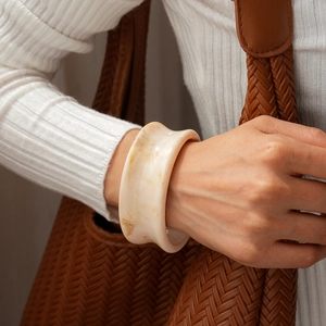 Détail macro de large bracelet manchette en résine marbrée crème porté par mannequin