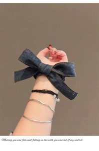 Détail d'un chouchou en jean bleu foncé et d'un bracelet en métal sur le poignet