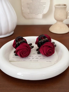 Detail of two wine red rose flower hair claws on a vintage background with a ceramic plate