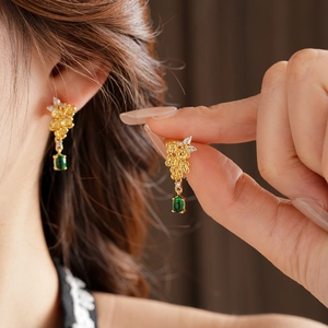 Détail de boucles d'oreilles fleur vintage dorées avec pierre verte et pompon