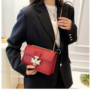 Detail of red snake pattern chain bag with golden bee buckle on black blazer