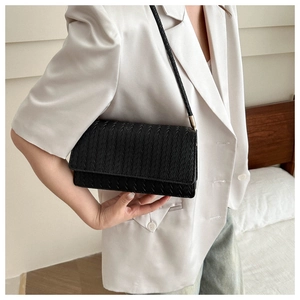 Close-up of black woven leather shoulder bag showing intricate texture on white blazer