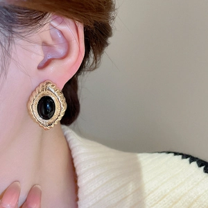 Close-up of vintage gold oval stud earrings with black gemstone worn by a model