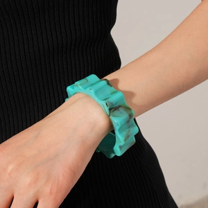 Detail of wavy mint green resin bangle with dark marble texture on model's wrist