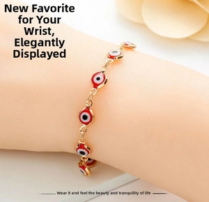 Nahaufnahme eines goldfarbenen Evil-Eye-Armbands mit roten Emaille-Anhängern am Handgelenk