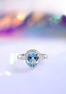 Macro shot of a pear-cut blue gemstone ring with a halo setting and curved silver band
