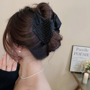 Detail of a large black acrylic hair claw clip with rhinestones worn on a hair bun