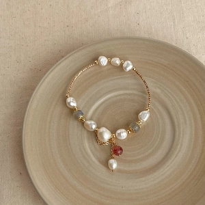 Detailed view of baroque pearls with red and grey beads on a gold bracelet chain