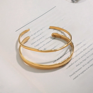 Close-up of gold stainless steel bangle with irregular ripple texture on white paper