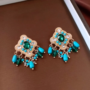 Macro detail of vintage bohemian drop earrings with emerald stones and glass tassels