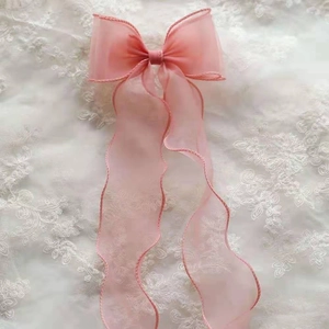 Detailed close-up of pink organza bow hair clip with long ribbons on lace background