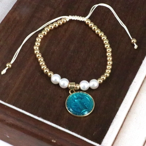 Bohemian handmade beaded bracelet with blue religious medal and gold beads on white cord