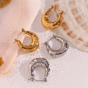 Detailed view of U-shaped gold and silver hoop earrings on a decorative beach background