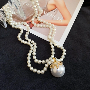 Close-up of double-layer pearl necklace with a starfish-shaped golden teardrop pendant