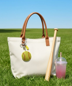 Glittery yellow softball keychain with tassel hanging on white canvas tote bag