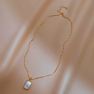 Elegante vergoldete Halskette mit quadratischem Perlmuttanhänger auf Satinhintergrund