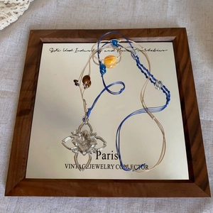 Detail view of woven blue and beige necklace with silver floral pendant and colored beads