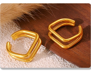 Detailed close-up of gold-plated square double-layered clip-on earrings on textured fabric