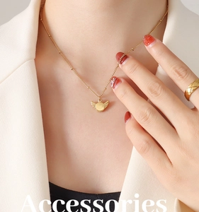 Close-up of gold wing pendant necklace and quilted ring on model in business attire