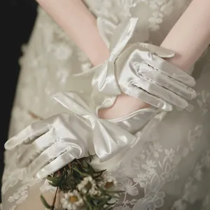 Close-up of elegant white satin bridal gloves featuring a decorative silk-like bow detail
