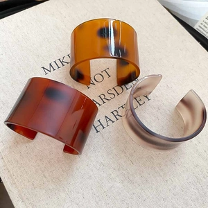 Three acetate cuff bracelets with amber tortoise pattern on a minimalist book background