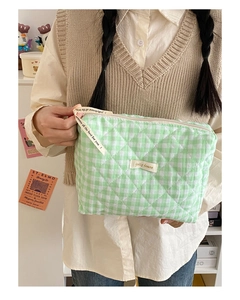Détail d'une trousse de maquillage matelassée à carreaux vert clair tenue à la main