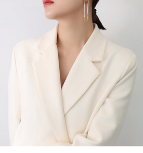 Detail of elegant gold U-shaped earrings with pearls paired with a cream blazer
