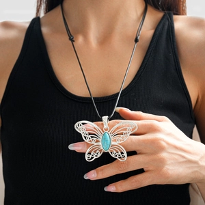 Detailed view of a silver hollow butterfly pendant with turquoise stone on black cord