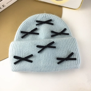 Detailed view of light blue knitted hat with black velvet bows on a gold tray backdrop