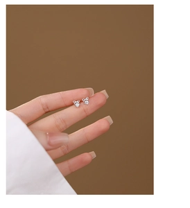 Macro shot of silver bow stud earrings with sparkling cubic zirconia on fingertips