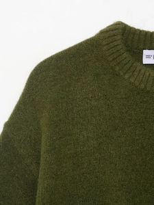 Détail macro du pull en maille vert forêt montrant la texture douce brossée et le col