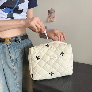 Macro shot of opening a beige quilted cosmetic bag with black bow embroidery details