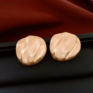 Close-up of matte gold textured oval wavy stud earrings on a leather display