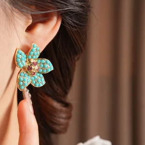 Close-up of vintage floral stud earrings with blue petals and red gem center on model