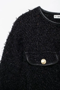 Gros plan sur une veste en tweed noir avec bordure en similicuir et bouton doré