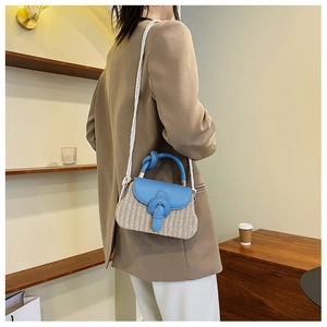 Detail of straw square bag with blue leather flap and woven strap shown on model