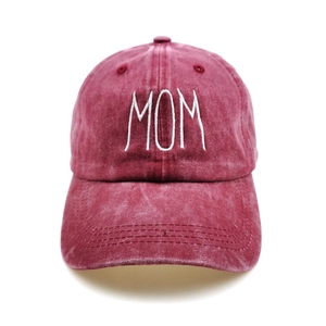 Close-up of white MOM script embroidery on washed burgundy cotton baseball cap texture