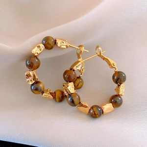 Detailed shot of golden hoop earrings with tiger eye stones on beige silk background