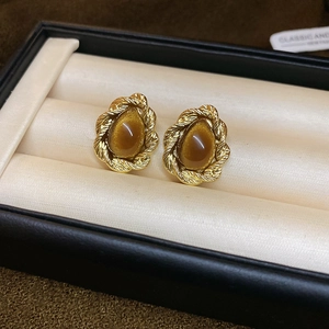 Detail of vintage gold-plated oval tiger eye stud earrings on beige silk cushion