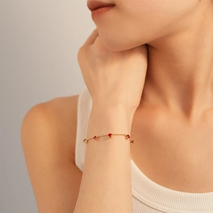 Detailed shot of delicate gold bead bracelet featuring five claw-set red zircons on a wrist