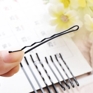 Hand holding a black wavy metal bobby pin for hair styling with multiple pins in background